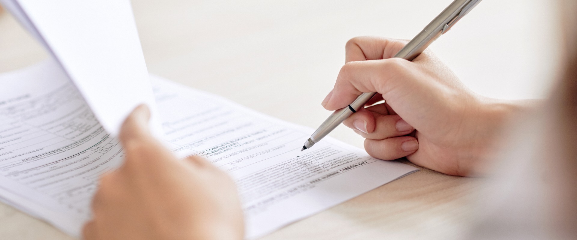 Crop shot of person with pen signing contract at desk in daylight