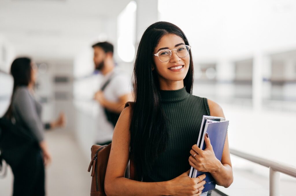 Portrait of young Brazilian student with backpack carrying books in college.