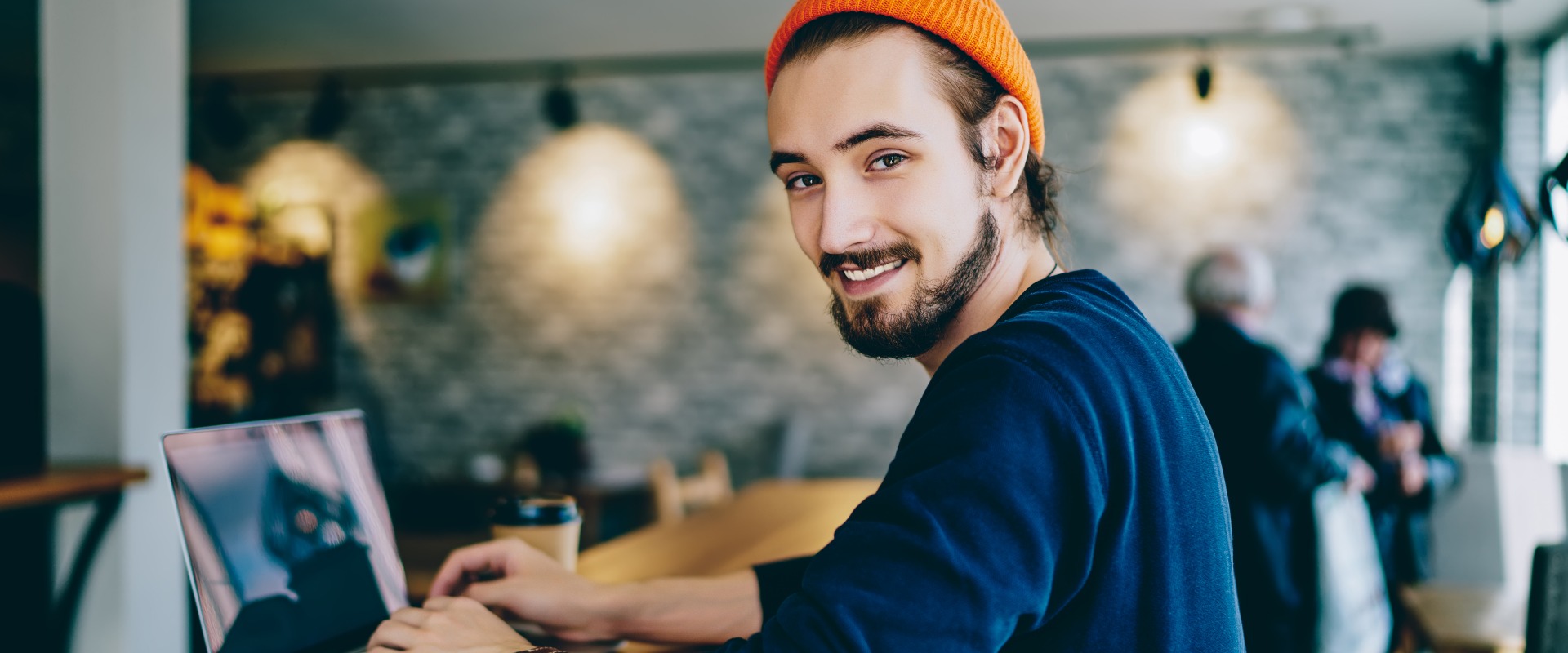 Skilled male it developer looking at camera coding on modern laptop computer working on freelance in cafe interior, portrait of cheerful hipster guy using netbook for e learning satisfied with course.